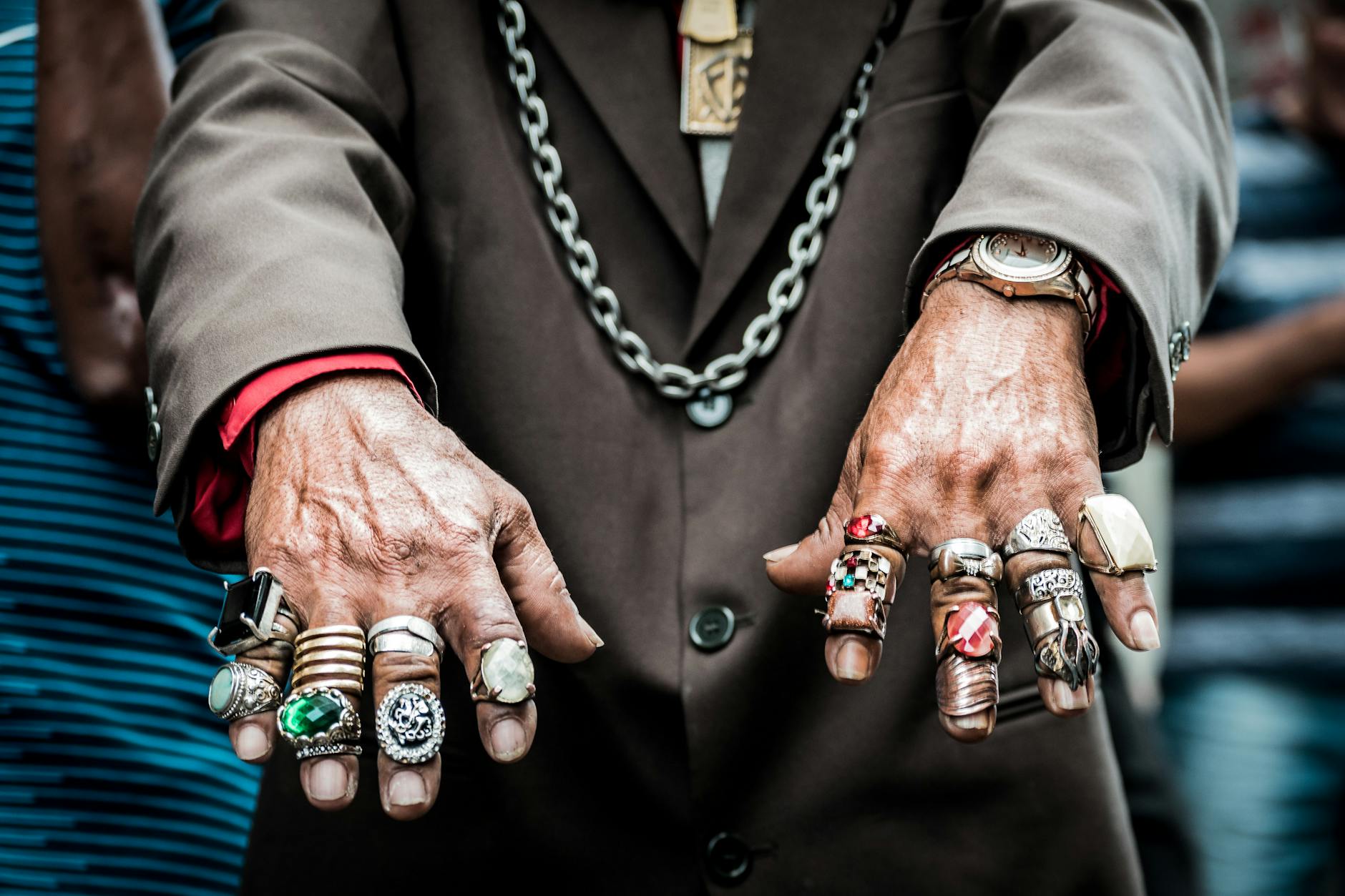 Dłonie w brązowej marynarce z kilkoma pierścionkami i naszyjnikiem