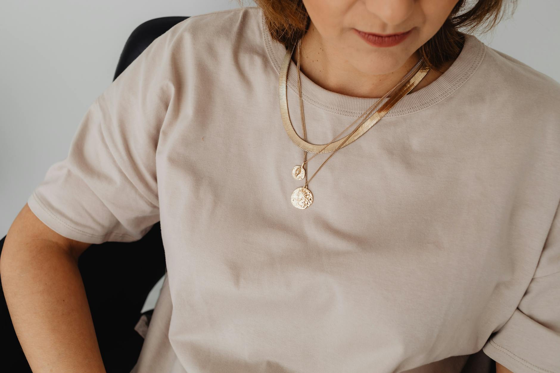Kobieta w beżowej koszuli z warstwowym złotym naszyjnikiem