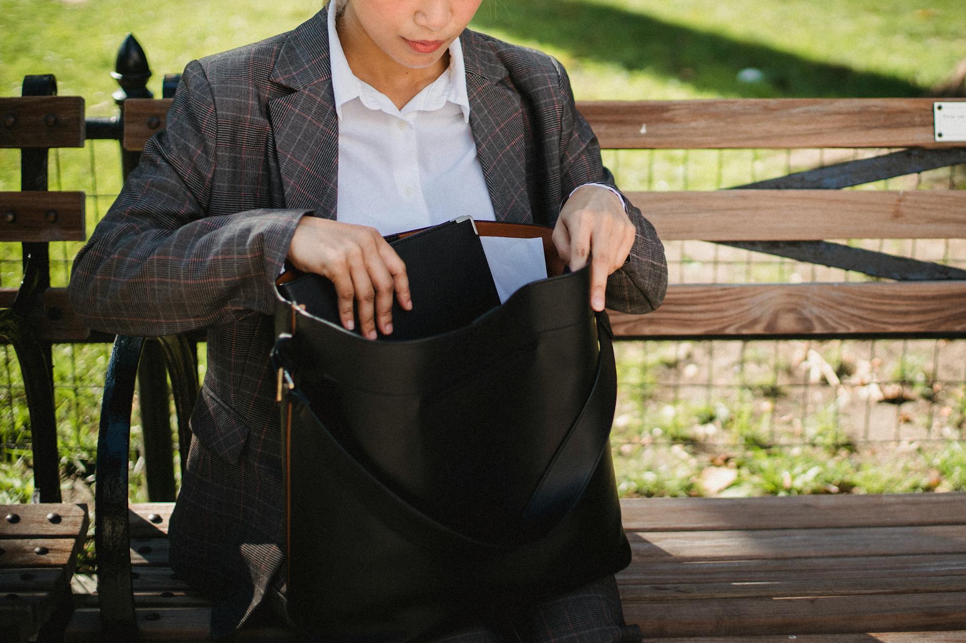 Kobieta w garniturze szuka kluczy w torebce na ławce w parku