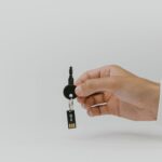 Dłoń trzyma brelok do kluczy z wbudowanym pendrive USB na tle jednolitym
