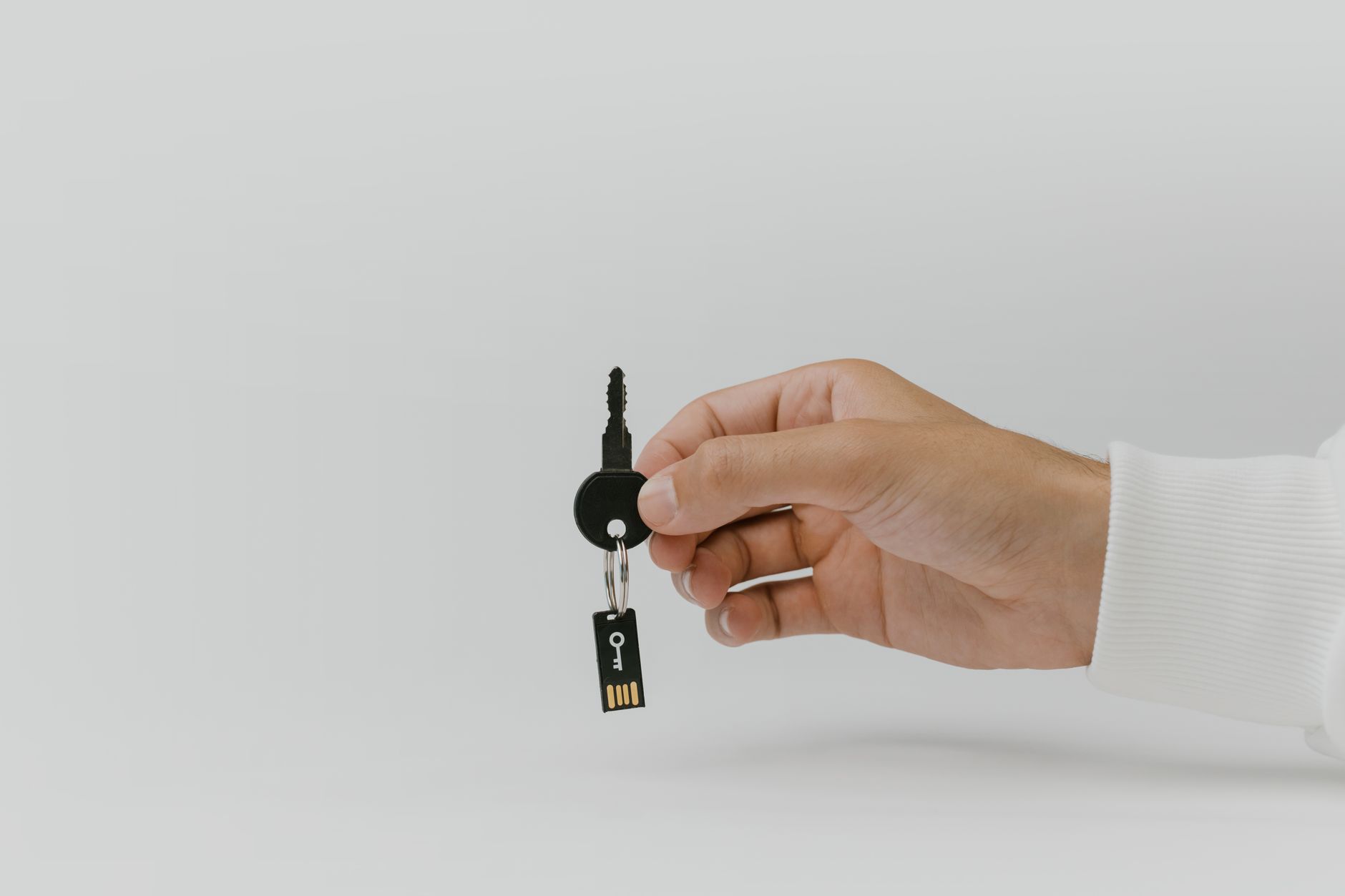Dłoń trzyma brelok do kluczy z wbudowanym pendrive USB na tle jednolitym